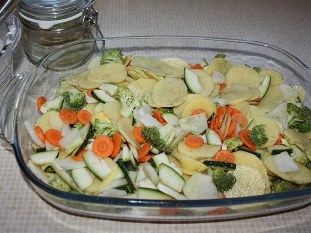 Vermenge das Gemüse für den veganen Kartoffelauflauf mit Kräutersalz.