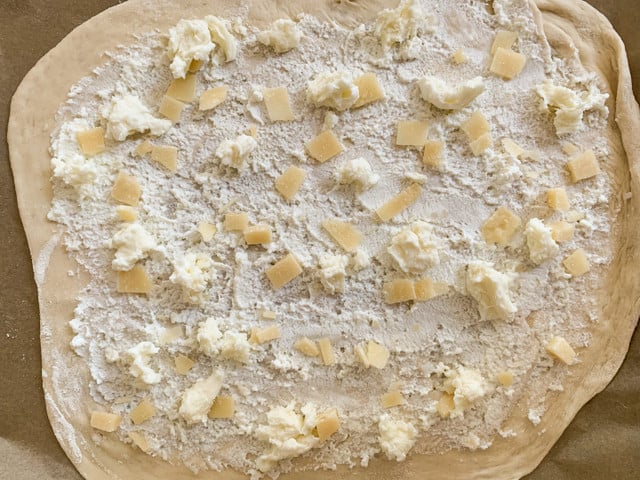Bestreiche den Teig dünn und verteile Parmesan und Mozzarella darauf.